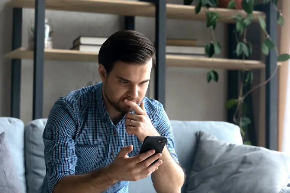 serieuze jonge man zit op de bank met telefoon in zijn hand