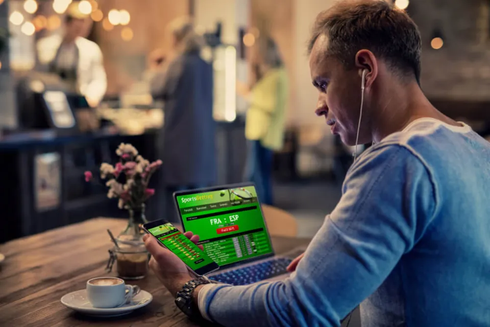man kijkt naar sportsbook op laptop en telefoon